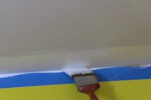 photo brushing white paint on ceiling along masking tape