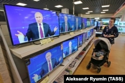 RUSSIA -- A woman walks past the TV screens in a shop during Russian President