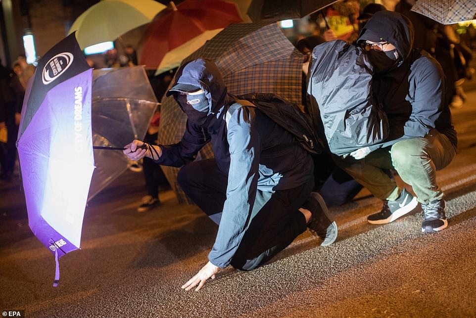 Protesters shield themselves behind umbrellas as Hong King police fire rounds of tear gas at them on Christmas Eve