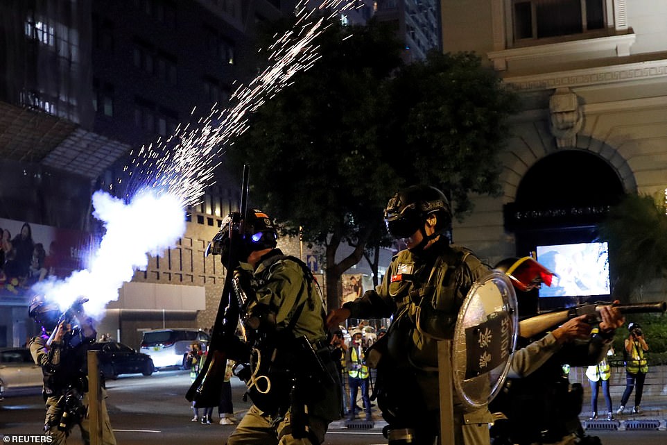 Hong Kong riot police officers stand on guard and fire shots of tear gas at anti-government protesters on the city streets