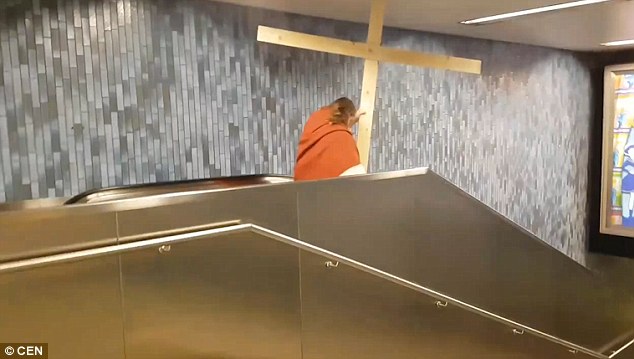 Keep the faith:  He starts to wiggle the cross out of the hole while continuing to walk on the escalator
