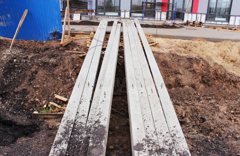 reinforced concrete beams of square section lie on the ground at the construction site near the house. royalty free illustration