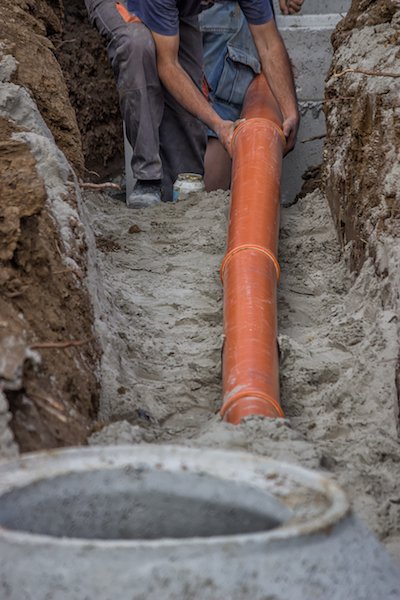 Прокладка и подключение рыжей канализационной трубы к бетонному колодцу